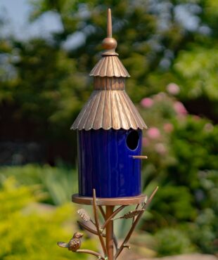 side view image of Iron and glossy cobalt blue porcelain birdhouse stake with ornate roof and a little bird perched on leaves attached to the stake
