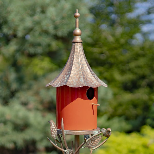 image of Iron and glossy orange porcelain birdhouse with funnel-shaped roof and a little bird perched on leaves attached to the stake