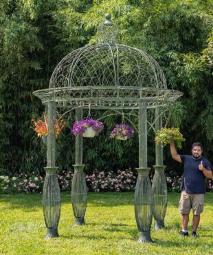 full size photo of 13 feet tall round metal garden gazebo in antique green distressed finish decorated with hanging flower pots in backyard, gentleman is standing near it