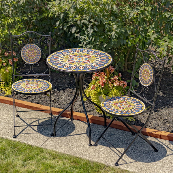 Bistro set of 3 pieces consists of 1 round table and 2 folding chairs decorated with mosaic tiles in blue, gold, red and yellow with iron black frame standing in garden