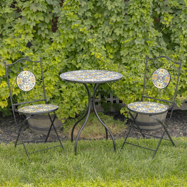 Bistro set of 3 pieces consists of 1 round table and 2 folding chairs decorated with mosaic tiles in blue, yellow, and green color palette with iron black frame standing in garden