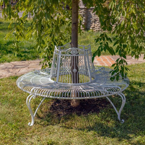 Victorian style round curved metal tree bench encircling the trunk of a tree in antique white distressed finish