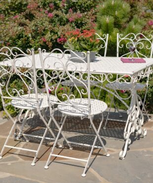 Metal dining set for 4 people consists of 4 chairs and 1 rectangular table in destressed antique white finish decorated with 2 clear vases with flowers