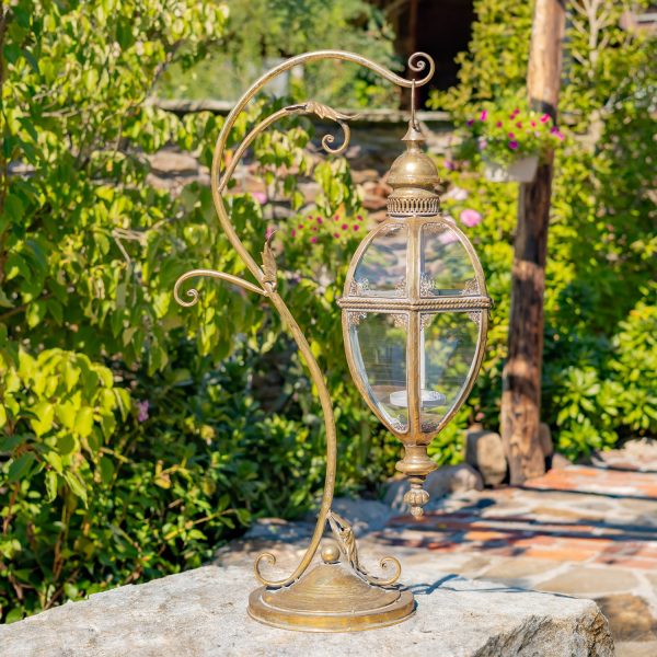 33.75 inch tall Victorian style metal hanging lantern with ornate stand in gold finish standing in garden