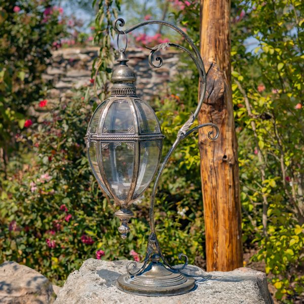 33.75 inch tall Victorian style metal hanging lantern with ornate stand in silver finish standing in garden