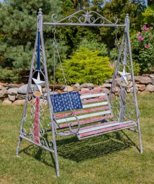 72 inch tall iron swing bench in American Flag style standing in beautiful garden