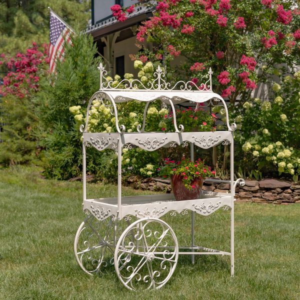 side view image of 6.5 feet tall iron ornate two-tier flower cart with two rotating wheels and handle in distressed antique white finish