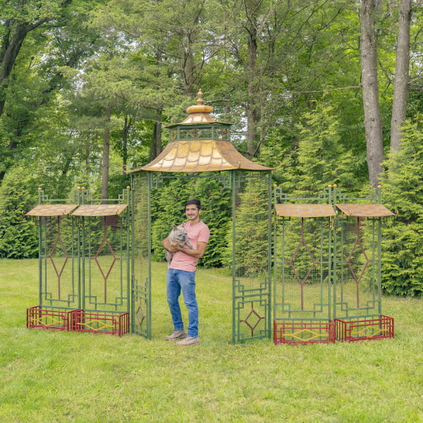 16 feet long iron garden gate in green and red colors with four side planters in Asian pagoda style with gold roof, young man standing in front with a dog