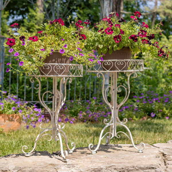 set of 2 ornate standing flower plant stand tables in 2 sizes in antique white finish standing in garden with flower pots