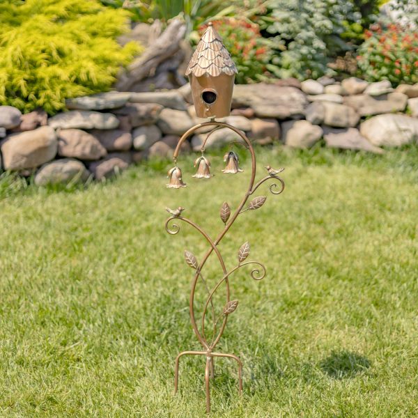 45 inch tall iron birdhouse on curved stake with bells in antique copper finish, standing in garden