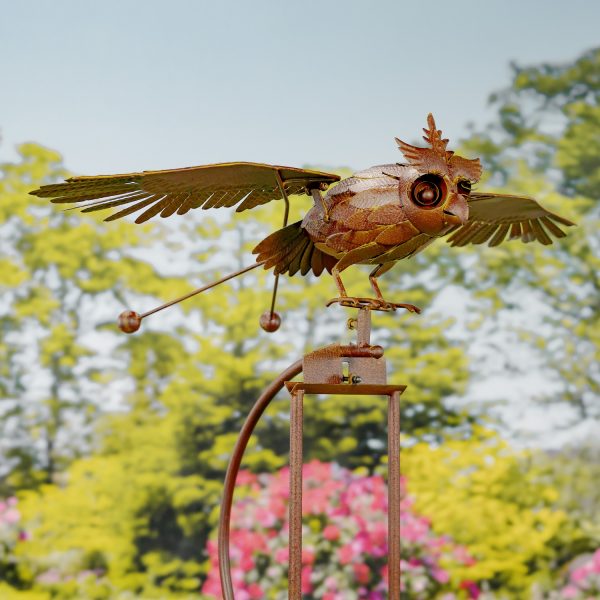 closeup of iron flying owl with flapping wings balanced on garden stake with ball anchor