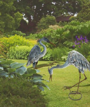 Two heron figurines displayed in a yard with a detailed hand painted design in colors blue-grey