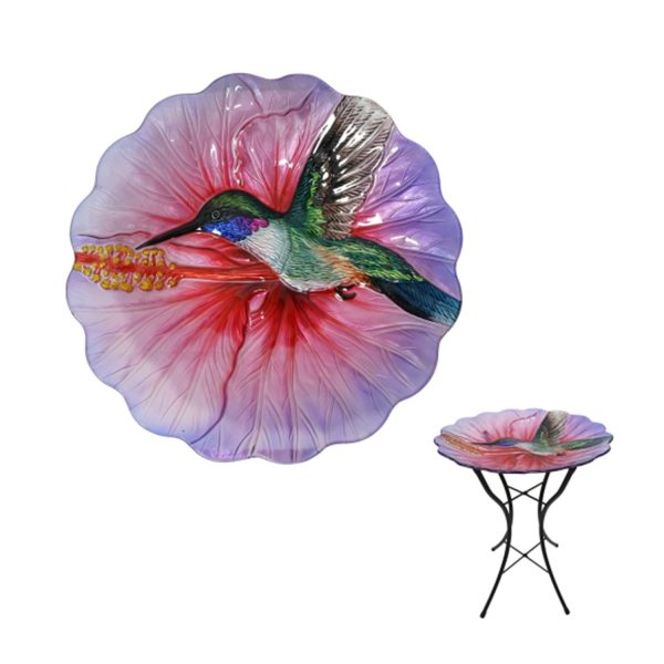 Glass birdbath with black stand, with a pink flower shaped bowl and humming bird.