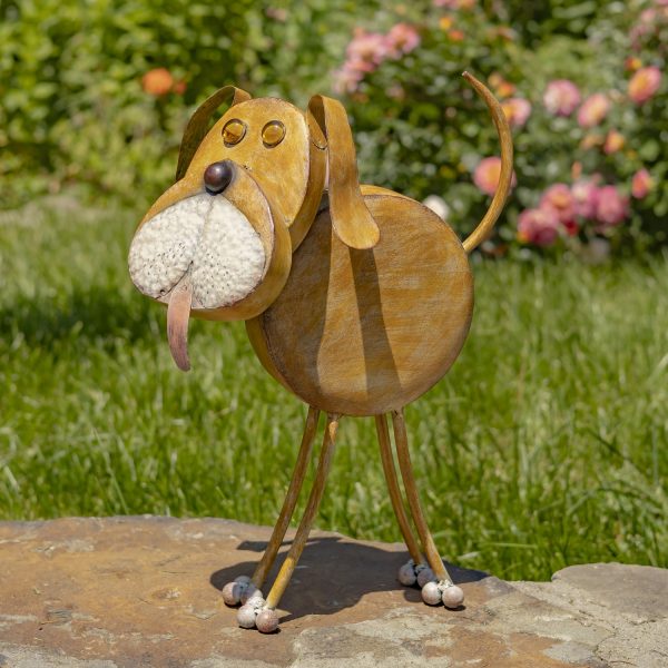 ChatGPT said: This is a whimsical 3D metal sculpture of a dog, about knee-high, with a round body, thin curved legs, and a tail raised in the air. Its large, textured snout is white, with a pink tongue playfully sticking out. The ears are long and floppy, and the eyes are small, raised circles. The sculpture has a warm, rusty brown hand-painted finish and stands on a flat stone surface in a sunny garden with green grass and blooming flowers behind it.