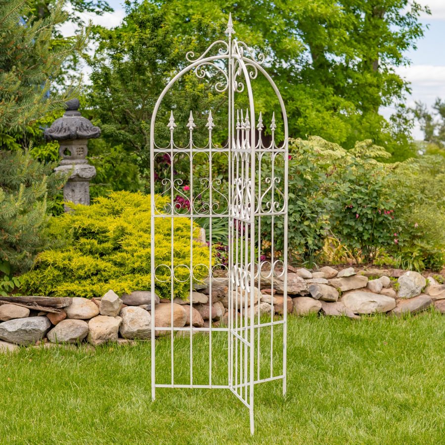Top of 7.7ft Tall Three Wall Folding Iron Trellis with Fleur-de-lis Accents Paris 1968 with a distressed, hand painted Antique white finish. Image shows the entire outdoor living structure displayed in a garden with beautiful flowers, landscaping and other outdoor décor in the background