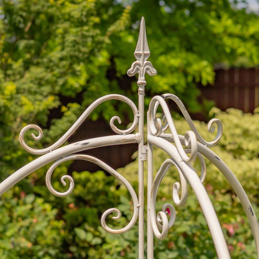 Top of 7.7ft Tall Three Wall Folding Iron Trellis with Fleur-de-lis Accents Paris 1968 with a distressed, hand painted Antique white finish. Image shows a closeup of the Fleur-de-lis detail at the top of the structure, bordered by iron flourish pieces.