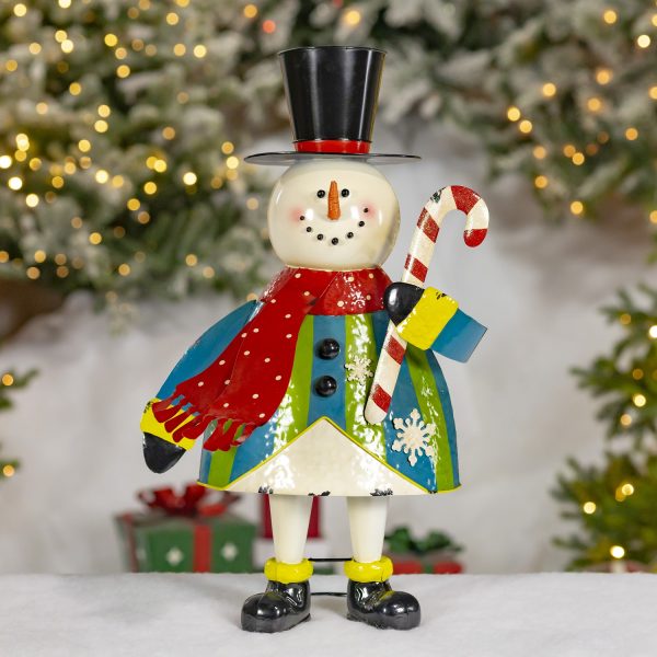 This is a cute snowman figurine with a smiling face, a carrot nose, and black button eyes and mouth. It wears a tall black top hat, a red scarf, and a colorful coat with blue, green, and white patterns, including snowflakes. The snowman is holding a red and white striped candy cane and has black boots on its feet.