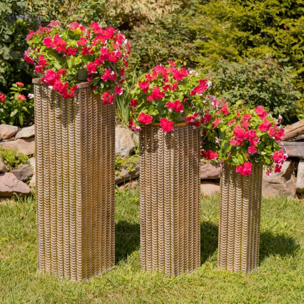 Three matching metal pedestal stands: tall rectangular columns with square, flat tops. They come in three heights—large, medium, and small—and are wrapped in a repeating raised, feather-like pattern. The finish is dark, aged gold.